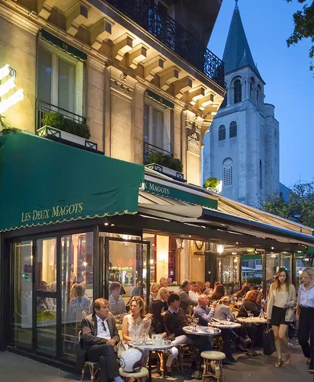 Café parisien animé en soirée avec terrasse.